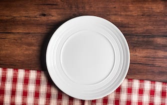 Empty white plate on a napkin on an old wooden brown background, top view. Image with copy space. Kitchen table with a towel and a plate - top view with copy space.