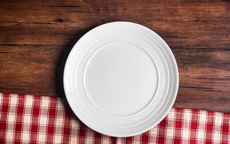 Empty white plate on a napkin on an old wooden brown background, top view. Image with copy space. Kitchen table with a towel and a plate - top view with copy space.