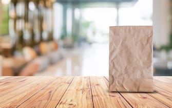 blank brown paper bag for taking away food on wood table blurred abstract background interior view for branding mockup packaging design