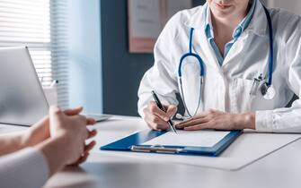 Doctor sitting at desk and writing a prescription for her patient