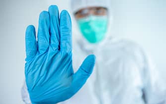 Male caucasian doctor wearing a protective suit and mask, making stop sign gesture, saysignaling No. Refusing virus disease, close up. Isolated on whi