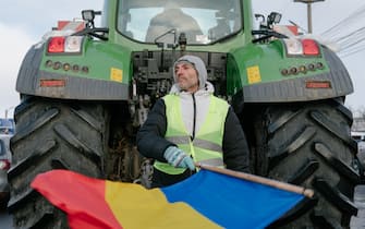 A demonstrator waves a Romanian national flag in front of a tractor during an anti-government protest by farmers and truckers in Afumati, on the outskirts of Bucharest, Romania, on Sunday, Jan. 21, 2024. Romania’s government approved a set of measures aimed at assisting farmers and truck drivers amid protests throughout the country that have blocked roads and customs for more than a week, but more is needed to meet their demands. Photographer: Andrei Pungovschi/Bloomberg