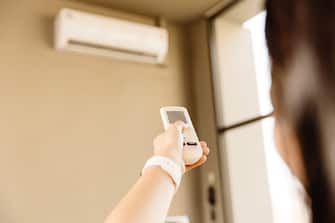Closeup people using remote control adjust room temperature in home office pointing to Air conditioner in hot summer season.