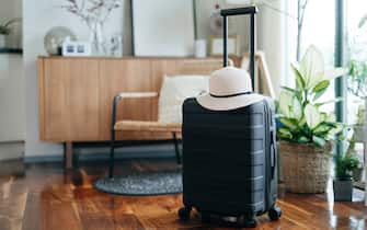 Still life of a black suitcase with a straw hat in the living room of an apartment. Travel and vacation concept