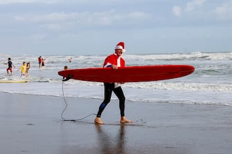 A surfer dressed as Santa carries a surfboard during the 15th annual "Surfing Santas" event in Cocoa Beach, Florida, on December 24, 2023. (Photo by Eva Marie UZCATEGUI / AFP) (Photo by EVA MARIE UZCATEGUI/AFP via Getty Images)