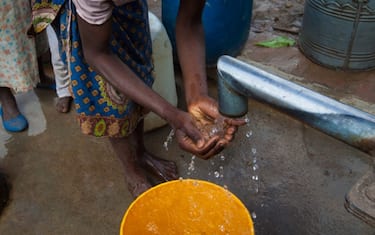 A young local girl, dressed in traditional clothing, washes her hands and drinks water from a borehole, in Nsanje District, southern Malawi. On the countryside of Malawi, people often have to walk long distances to get water from the nearest pump.