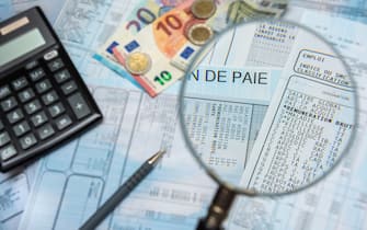 Blurred french payroll with a calculator, a pen, euro cash, and a magnifying glass. Sharp focus only through the magnifying glass