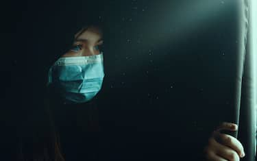 Teenage girl with blue eyes looking on the window in the darkness, mysterious concept