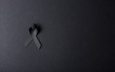 Black handmade awareness paper ribbon on black background.