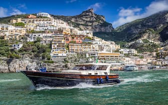 A small luxury motorboat takes tourists for a trip from the beautiful seaside town of Positano to the Island of Capri along the spectacular Amalifi Coast of Italy.   The Amalfi coast villages are just south of Naples and feature stunning drops from hill-hugging roads spotted with villages that are a favorite tourist destination for people around the world - including many celebrities!