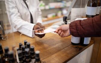 Cropped shot of a female chemist giving prescription to a customer in a pharmacy. Acrylic shield between on pharmacy checkout counter.