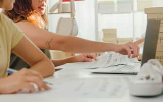 Closeup of young Asian women using laptop receiving purchase order and check product on stock work at shop. SME small business e-commerce concept.