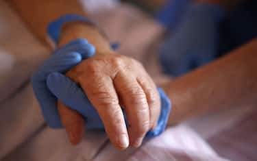 TOPSHOT - A nurs wearing protective gloves holds the hand of a patient in the palliative care unit of the the Eugenie Hospital in Ajaccio, on the French Mediterranean island of Corsica, on April 23, 2020, on the thirty-eighth day of a lockdown in France aimed at curbing the spread of the COVID-19 disease, caused by the novel coronavirus. - A message, a drawing or a picture slipped into the coffin, letters from caretakers to the families... Several "rituals" have been established in Corsica to deal with the deaths of COVID-19 patients deprived of their families, doctors told AFP. (Photo by Pascal POCHARD-CASABIANCA / AFP) (Photo by PASCAL POCHARD-CASABIANCA/AFP via Getty Images)