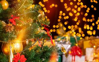 Stack of packed gift boxes under Christmas tree against particles lights. Lots of Christmas gifts under the tree. Selective focus on the yellow globe!