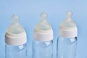 High angle view of three glass empty baby bottles ona a blue colored background.