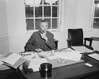 (Original Caption) 6/2/64-Princeton, New Jersey: Dr. J. Robert Oppenheimer, suspended Atomic Energy Commission consultant, smokes at his desk at the Princeton Insitute for Advanced Study. June 2nd, the day after it was revealed that a special AEC personnel and board voted 2-1 to make his suspension permanent. Dr. Oppenheimer refused comment on the board's ruling, but his counsel is planning to review the case before the full AEC.