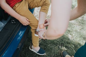 Woman applies a band aid to a little boys grazed ankle.