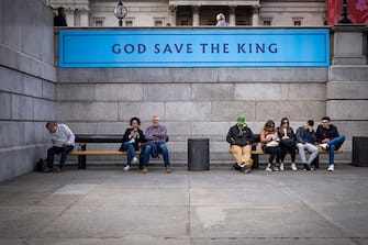 LONDON, ENGLAND - MAY 04:  People sit in Trafalgar Square beneath a banner declaring 'GOD SAVE THE KING' on May 04, 2023 in London, England. The Coronation of King Charles III and The Queen Consort will take place on May 6, part of a three-day celebration. (Photo by Christopher Furlong/Getty Images)