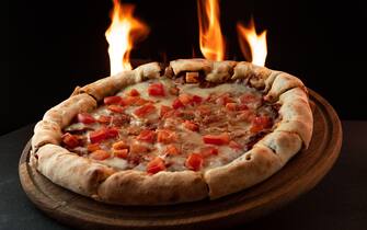 Neapalitan pizza with tomatoes on dark background with fire. Cooking pizza on fire. Pizza with flames in the background