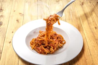 spaghetti egg based (Italian tagliatelle) topped with meat and tomato sauce, steamed in a plate on rustic wooden background