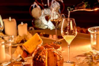 champagne is poured into glass on table set in Christmas style with  blurred panettone and candles, warm mood light