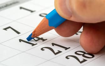 Man holding a pencil in his hand and recording his schedule on a desk calendar