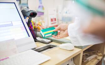 Cropped image of male pharmacist scanning medicine box with bar code reader. Chemist is working at checkout counter. He is at pharmacy.