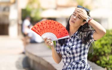 Woman uses hand fan to cool down when summer heat wave hits the city.