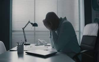 Stressed exhausted doctor sitting at office desk and resting with head in hands, burnout in healthcare concept