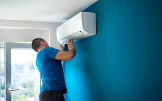Closeup side view of a trained professional installing an indoor unit of a split AC system.