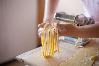 Hands of woman making some Italian tagliatelle with pasta machine.