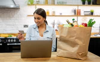Happy woman at home buying groceries online on her laptop computer and paying by credit card