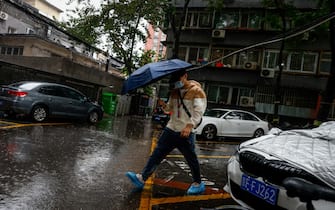 epa10776422 A man uses an umbrella during a downpour in Beijing, China, 30 July 2023. China's National Meteorological Center issued a red alert, the highest alert in multiple provinces including Beijing, as the country is expected to continue experiencing heavy rainfall brought by Typhoon Doksuri.  EPA/MARK R. CRISTINO