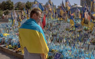 A man wrapped in a national flag visits a designated area for commemorating fallen Ukrainian and foreign fighters, during the Independence Day of Ukraine, in the Independence Square in Kyiv, on August 24, 2024. (Photo by Roman PILIPEY / AFP) (Photo by ROMAN PILIPEY/AFP via Getty Images)