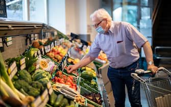 Senior man with face mask buying vegetables in a local supermarket. Elderly man doing home shopping in grocery store with a shopping cart.