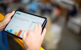 Close up of male hands working on a digital tablet in warehouse. Worker reviewing statistical graphs on tablet computer.