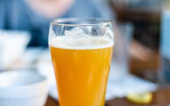 A close up of the top portion of a warm, orange toned glass of a hazy IPA, India Pale Ale, beer, with foam on the glass