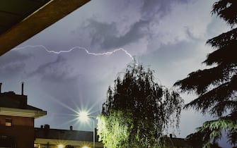 Lightning in the sky between the roofs of condominiums during the summer storm in Milan on April 7, 2023