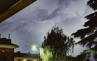 Lightning in the sky between the roofs of condominiums during the summer storm in Milan on April 7, 2023