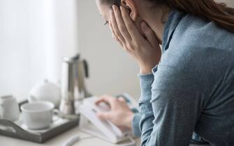 Sad depressed woman at home sitting on the sofa, she is calling an help line with her phone