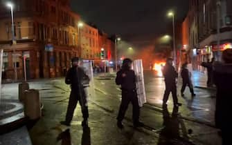 This video grab taken from an AFPTV video shows Irish Garda riot police forming a cordon around a burning police car, on Parnell Street in Dublin on November 23, 2023, as people took to the streets following the stabbings earlier in the day. Five people, including three children, were taken to hospital on Thursday, Irish police said, following a suspected stabbing outside a Dublin school. Police declared a major incident and threw up a cordon around Parnell Square in the heart of the Irish capital but said they do not suspect a terror motive. (Photo by Peter MURPHY / AFP)