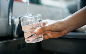 Close up of a woman's hand filling a glass of filtered water right from the tap in the kitchen sink at home