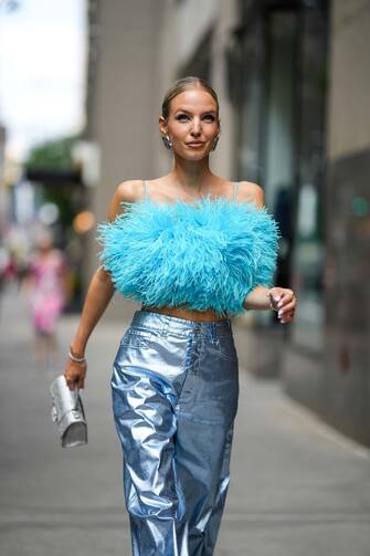 NEW YORK, NEW YORK - SEPTEMBER 13: Leonie Hanne wears silver and diamonds B logo earrings from Balenciaga, a pale blue feathers cropped tank-top, blue shiny metallic large pants, a silver sequined Hourglass handbag from Balenciaga, gold bracelets, a silver and gold watch, a gold Juste Un Clou ring from Cartier, outside Brandon Maxwell, during New York Fashion Week, on September 13, 2022 in New York City. (Photo by Edward Berthelot/Getty Images)
