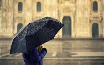 Girl with heavy jogger in winter sheltering from snow and rain at night illuminated by lampposts with an umbrella. In the city of Milano, Italy