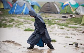 A refugee walks through the mud during a downpour in the refugee camp at the border between Greece and Macedonia in Idomeni, Greece, 13 March 2016. After the closing of the Balkan route, around 12,500 refugees are now living in this camp. Photo: KAY NIETFELD/dpa