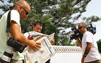 Reporters and photographers read the newspapers as they wait outside the rented villa of Kate and Gerry, parents of missing four-year-old Briton Madeleine McCann, in Praia da Luz, in southern Portugal 09 August 2007. Portuguese and British newspapers report that during a review of evidence sniffer dogs from the British police found traces of blood and the odor of a corpse inside the room from which Maddie went missing in May. Madeleine McCann by this weekend will have been missing for 100 days from a hotel room in the southern Portuguese resort where she and her two-year-old twin siblings were sleeping while her parents were dining at a nearby restaurant. AFP PHOTO / POOL/ STEVE PASRONS (Photo credit should read Steve Parsons/AFP via Getty Images)