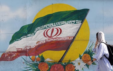 epa10295546 A woman walks past a graffiti showing the Iranian national flag in Tehran, Iran, 09 November 2022. Iran has been rocked by anti-government protests, with supporters worldwide, following the death in September 2022 of Masha Amini, a 22-year-old girl who died while in police custody after being detained for breaking Iran's strict dress code for women. Iranian leaders condemned the protests and accused the United States and Israel of planning the uprising.  EPA/ABEDIN TAHERKENAREH