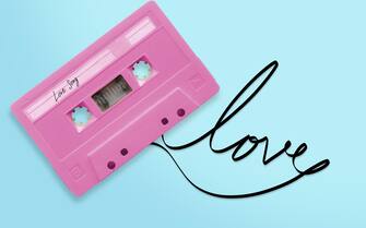 Frasi San Valentino pink audio cassette tape with label tag love song tangled tape ribbon word love isolated on blue background, top view.