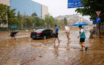 epa10779160 People walk near a car stuck in muddy road during a downpour in Mentougou District, west of Beijing, China, 01 August 2023. Heavy rains brought by Typhoon Doksuri caused floods in northern China and left two dead and thousands being evacuated as Beijing experienced its heaviest rainfall of the year.  EPA/MARK R. CRISTINO