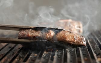 Chef cooking steak on a grill with smoke sizzling off the grill with dramatic lighting.